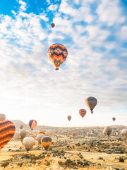 Flying in sky many bright colored beautiful balloons into air in Cappadocia in mountains early at sunrise, dawn. Filling balloon with hot air from burner, big basket. Tourists excursion, cloud flight