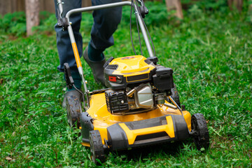 lawn mower in the garden. Yellow lawn mower on a background of green grass. Mowing grass in the garden with a lawn mower.