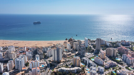 Aerial view of the Portuguese city of Portimao with high-rise buildings on the coast with beaches. Tourist cruise liner in the background in the sea.