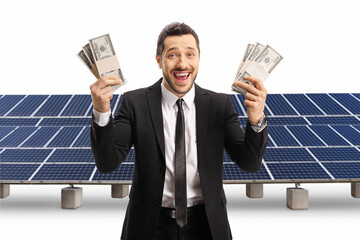 Excited man in a black suit holding stacks of money in front of a solar farm