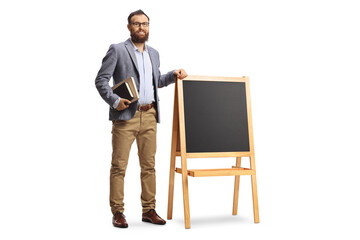 Full length portrait of a bearded male teacher standing next to a blackboard with books in his hands