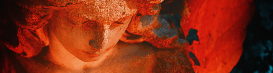 Beautiful angel on a cemetery against the background of leaves. Fragment of ancient statue....