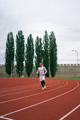 Fototapeta premium Motivated determined young male athlete running on red race track while training at sports stadium in city 