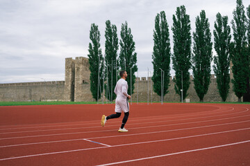 Motivated determined young male athlete running on red race track while training at sports stadium...