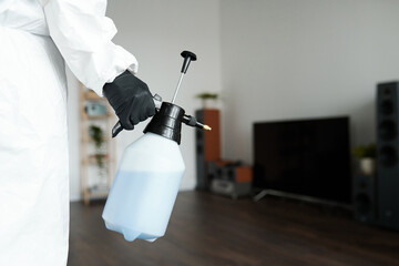 Close-up of cleaning worker in protective suit using sprayer with detergent while doing housework