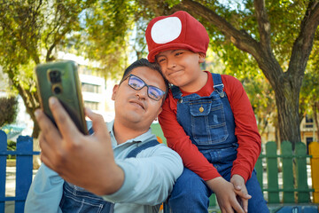 latin father and son taking a selfie together in an outdoor park in video game clothes in the city...