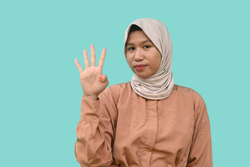 A calm Asian teenager wearing a brown t-shirt giving number 12345 by hand gesture on blue background. 