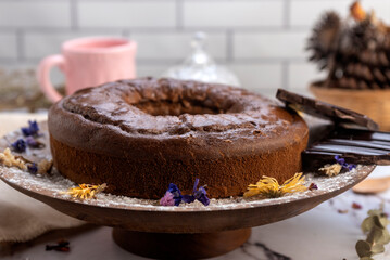 round chocolate cake with chocolate bar and covered in liquid chocolate and decorated with dried flowers and portion of cake served on a plate