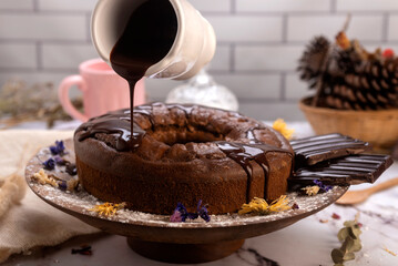 round chocolate cake with chocolate bar and covered in liquid chocolate and decorated with dried flowers and portion of cake served on a plate