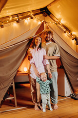 Happy family with lovely baby relaxing and spend time together in glamping on summer evening. Luxury camping tent for outdoor recreation and recreation. Lifestyle concept