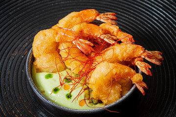 Shrimp tempura on a plate placed against a black background.