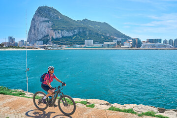 Fototapeta premium happy senior woman cycling with her electric mountain bike below the Rock of Gibraltar, Andalusia, Spain