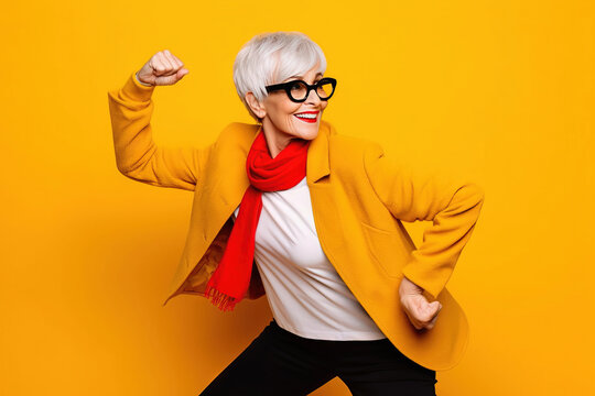 smiling grandmother with glasses doing poses on a studio with yellow background
