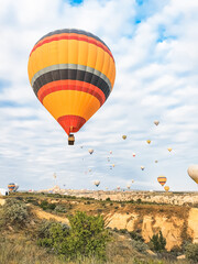 Fototapeta premium Flying in sky many bright colored beautiful balloons into air in Cappadocia in mountains early at sunrise, dawn. Filling balloon with hot air from burner, big basket. Tourists excursion, cloud flight