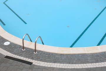 Swimming pool stone pavement tiles stone paving poolside background blue water surface. Ladder pool border. Edge pool stair