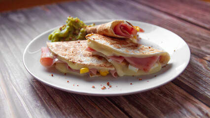 A plate of food with a quesadilla and guacamole on it.