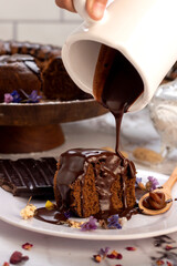 round chocolate cake with chocolate bar and covered in liquid chocolate and decorated with dried flowers and portion of cake served on a plate