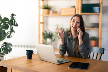 Happy smiling businesswoman wearing casual clothes and using modern smartphone in her home office at early morning, successful female employer to make a deal while sitting at her working space