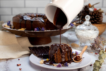 round chocolate cake with chocolate bar and covered in liquid chocolate and decorated with dried flowers and portion of cake served on a plate