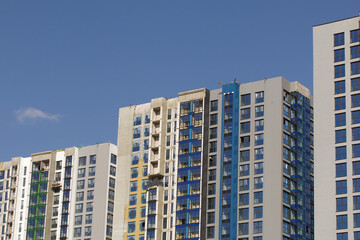 Fototapeta premium Modern high-rise buildings made of concrete and glass. Color design of facades. Construction site. The final stage of construction. Against the background of the blue sky.