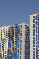 Modern high-rise buildings made of concrete and glass. Color design of facades. Construction site. The final stage of construction. Against the background of the blue sky.