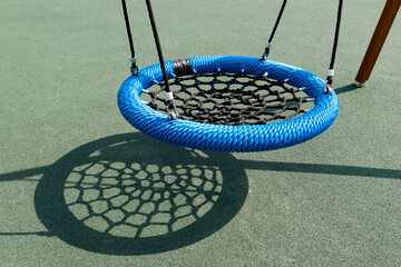 Outdoor swing with wicker round seat on green artificial ground. School playground