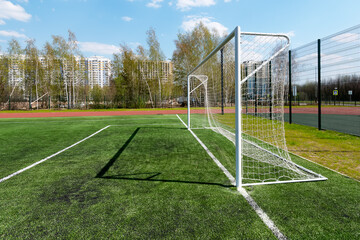 Football goal on a school soccer field with artificial grass against a blue sky