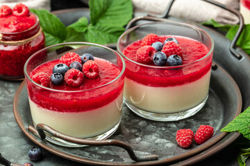 Raspberry Panna cotta with raspberry jelly on a dark background. Berry dessert with cream sauce in small jars. place for text