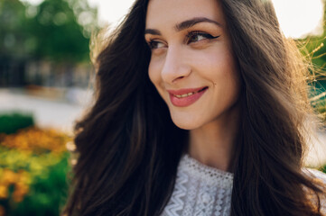 A boho brunette with lush hair is posing outside on a sunny summer day.