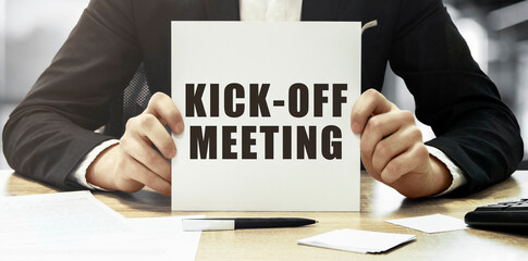 Businessman holding a white card with text Kick off meeting on office background