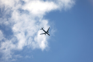 Silhouette of airplane flying in sky with white clouds. Passenger plane at flight, travel concept