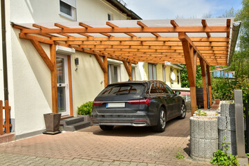 Moderner Carport aus lasiertem/lackiertem Holz im Einfahrtsbereich eines Wohnhauses