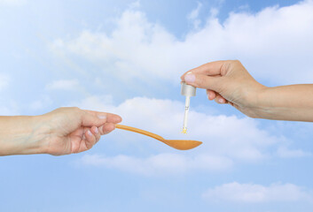 Health and medical concept. Health care with vitamin D3. Woman's hands holding spoon and dropper pipette with liquid vitamin D3 on sky background.