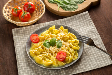 Pasta in a creamy sauce with cheese with a fork next to tomatoes, a knife and greens on a linen napkin.