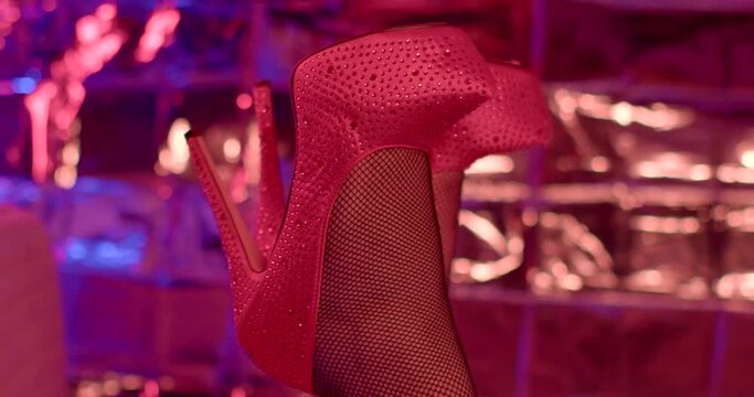 Red shoes on the legs of a woman in the night red light. She moves her leg in anticipation of a date. Demonstration of small traits of behavior when meeting a lady. Soft focus. female domination
