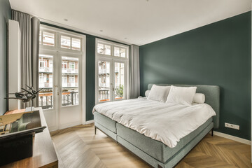 a bedroom with green walls and white bedding, hardwood flooring in the room is very well lit by large windows