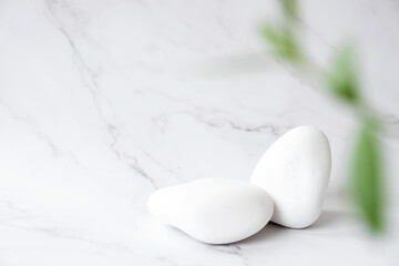 White stone product display platform with green leaves in defocus. White podium on marble background. Podium, stage pedestal or platform. Trendy natural mockup template. Free space.
