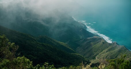 Mountain ranges in dense foggy haze at dawn. Thick clouds descends from the peaks to the ocean coastline.
