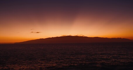 Island silhouette in ocean in magical sunset lilac light. Sky glows like in a fairy tale. La Gomera, Canary, Spain. Dark sea water at dusk.