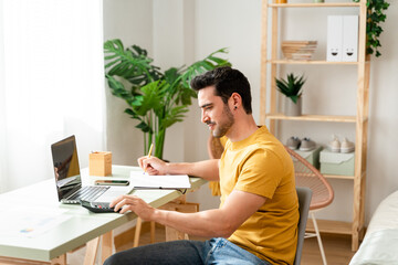 Man sitting at desk at home doing bills with calculator.