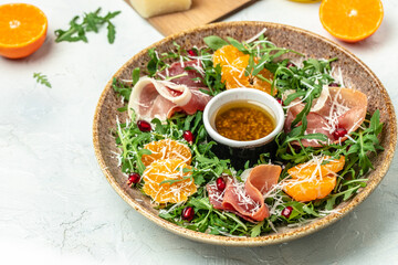 Delicious salad with arugula mandarins, prosciutto jamon and Parmesan cheese on light background. Long banner format. top view