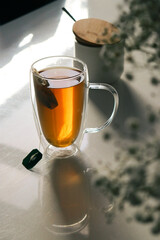 black tea in a glas cup on white table and flowers, blurred background 