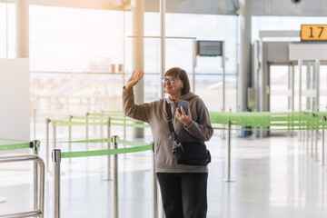 Happy smiling mature traveler woman hold smartphone and wave hand in greeting someone who meeting...