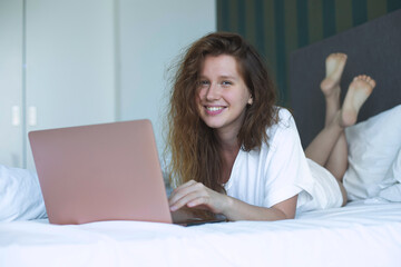 young woman lies and use laptop in bed in the morning. concept online learning, work, shopping
