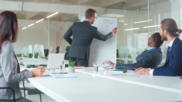 Young businessman providing training about increasing sales productivity of company for managers. Multiethnic workers actively discussing and listening important lecture. Planning success strategy.