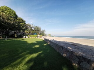 Tourist attraction Hua Hin beach, Thailand in December. Brown sand beach. The clear blue sky saw streaks of white clouds. There are trees and lawns to provide shade. Bright sunlight and breeze.