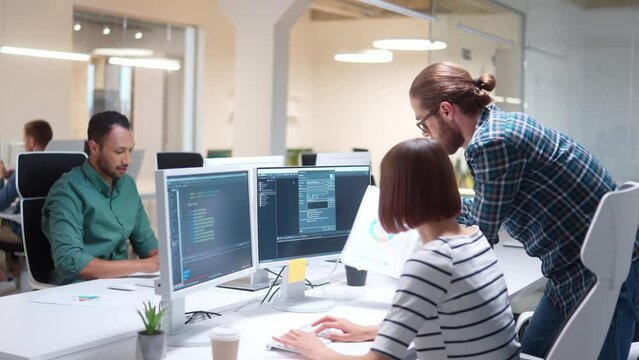 Group of multiethnic developers working with big data. Handsome man with glasses supporting or advising female programmer. Focused looking at multiple screens and discussing about programming server.