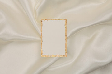 Gold glitter empty canvas paper frame on beige silk fabric background. Abstract copy space texture.