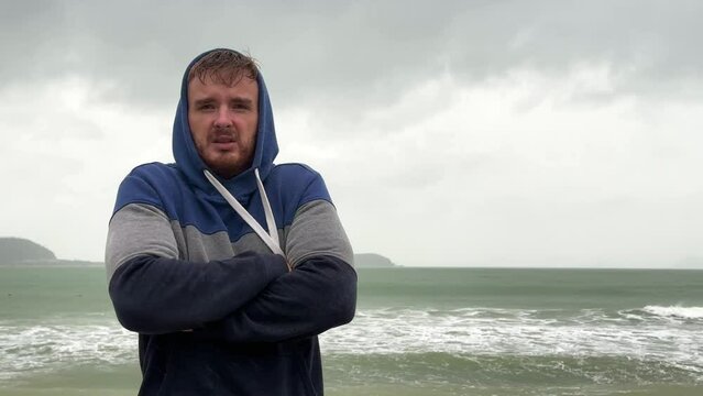 Portrait of unhappy depressed frozen trembling guy, young shivering from cold sad upset man on the sea beach, suffering from bad weather on summer vacation 