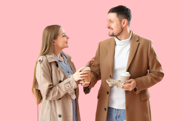 Young man giving cup of coffee to his wife on pink background